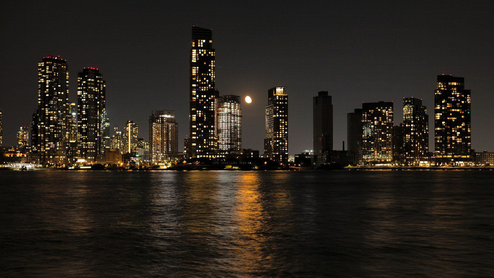 City skyline at night with a full moon over the water