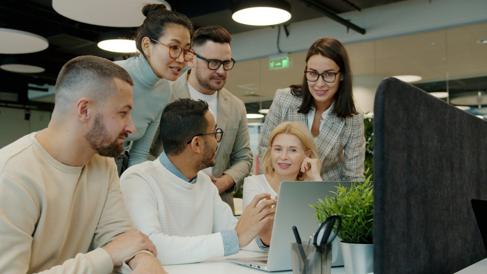 Smiling colleagues gathered around a laptop in an office