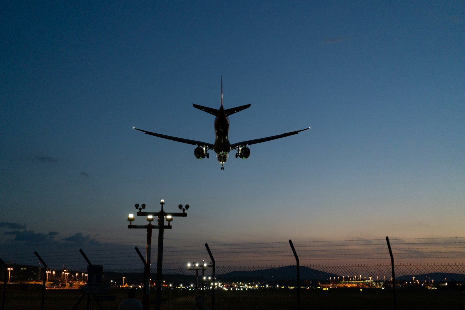 Airplane flying over runway lights at dusk